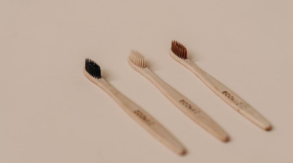 três escova dentais feita de bambu. a escova da esquerda tem cerdas pretas a escova do meio tem cerdas cor creme e a escova da direita tem cerdas marrons.