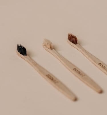 três escova dentais feita de bambu. a escova da esquerda tem cerdas pretas a escova do meio tem cerdas cor creme e a escova da direita tem cerdas marrons.