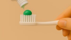 a mão de uma pessoa segurando uma escova dental branca e colocando um creme dental verde