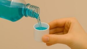 mão de uma pessoa segurando a tampa e enchendo com enxaguante bucal de coloração verde