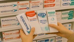 mão de uma pessoa segurando 4 embalagens de cremes dentais para sensibilidade